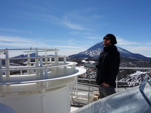 Junger Mann mit Sonnenbrille und Mütze, im Hintergrund ein großer Berg und blauer Himmel