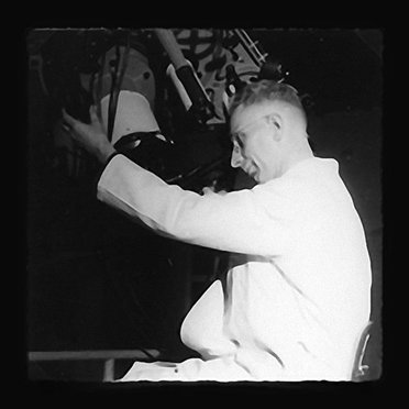 Man in white coat looks through telescope